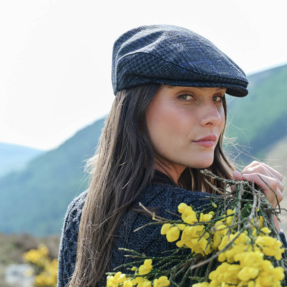 Woman wearing a flat cap holding yellow flowers with mountains in the background