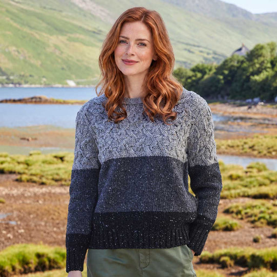 Image featuring The McConnell Goleen Sweater in grey, crafted with authentic Irish knit textures, traditional cable knit detailing, and a contemporary colour-block design in shades of grey, showcasing modern Irish craftsmanship against a rugged coastal landscape.