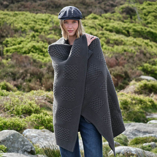 Woman wearing a dark gray knitted blanket and flat cap in a natural setting