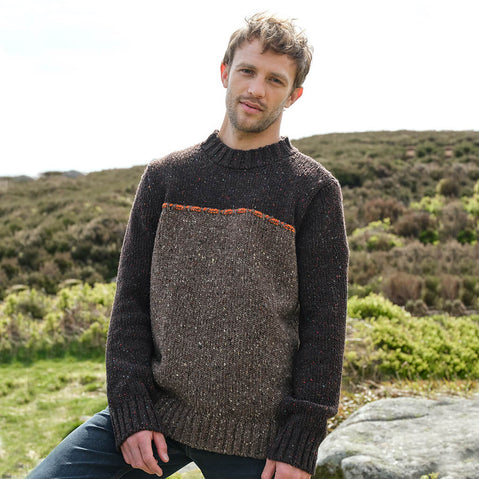 Man wearing a brown knitted sweater sitting outdoors with greenery in the background