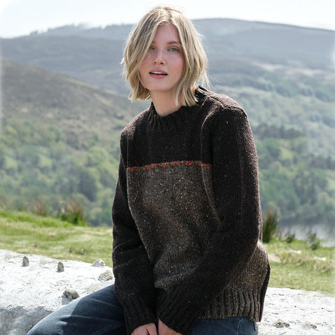 Woman wearing a dark brown sweater sitting outdoors with mountains in the background