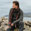 Men's Alpaca Islander Scarf in Cranberry, crafted from luxuriously soft alpaca wool with a rich textured weave, styled with traditional Irish knitwear against the rugged Irish coastline for a timeless heritage look.