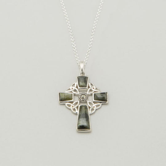 A silver Celtic cross pendant hangs from a delicate chain. The cross features intricate knotwork and a sun design at the center. The background is neutral, highlighting the pendant's details.