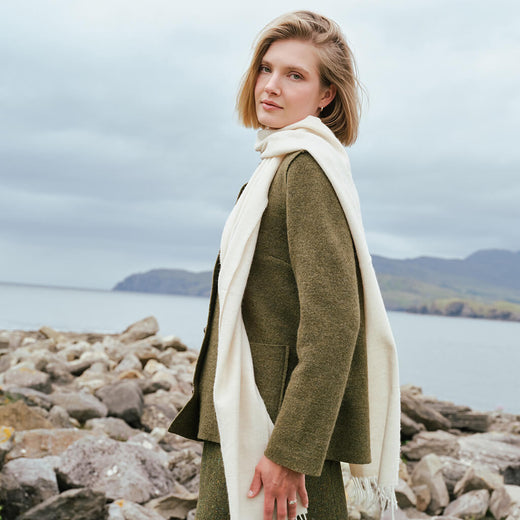 Ladies Herringbone Lambswool Scarf in Beige, crafted from luxuriously soft lambswool with a timeless herringbone weave, styled by the Irish coastline for an elegant and classic cold-weather look.