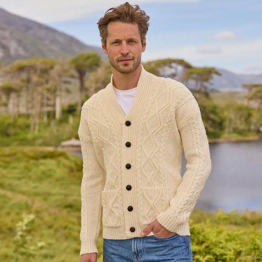 Man wearing a cream The Irish Store Men's Classic Aran Cardigan with black buttons in a scenic outdoor setting.