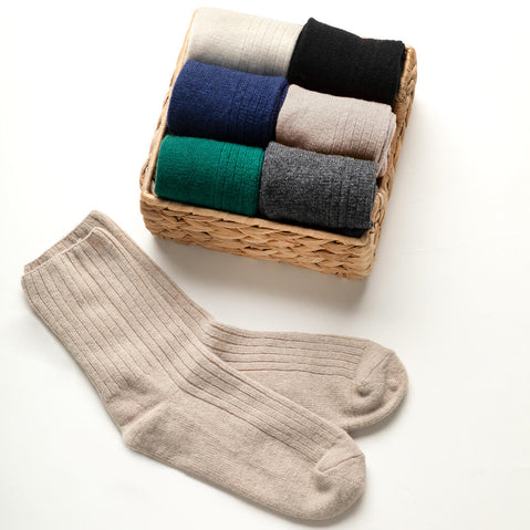 Wicker basket with assorted colored socks and a single beige sock on a white background