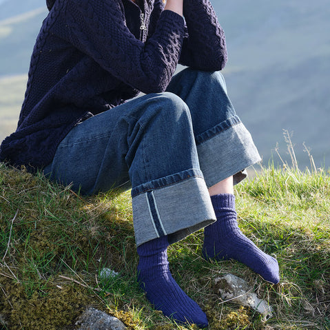 Person sitting on grass wearing a dark coat, jeans, and blue wool socks.