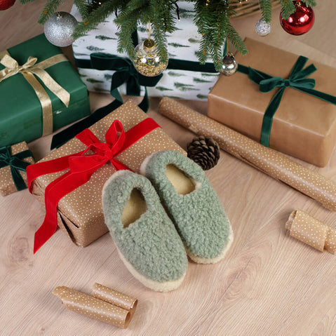 Merino Wool Slippers in mint green with fuzzy texture and cream soles displayed among wrapped Christmas gifts, pine garland, ornaments, and gold wrapping paper