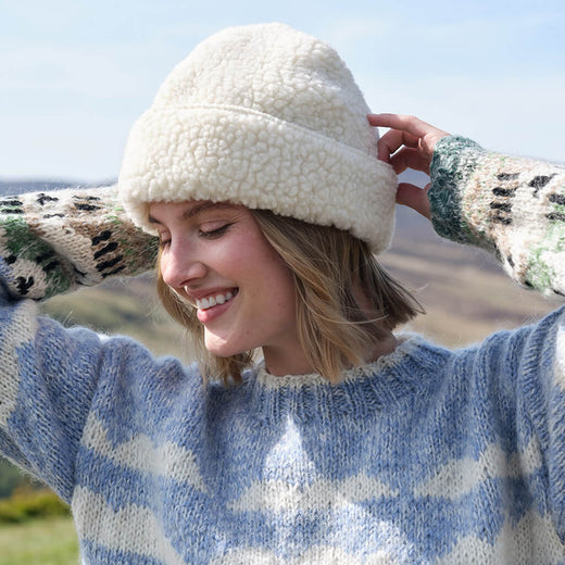 Woman wearing a white fleece-lined hat and patterned gloves outdoors