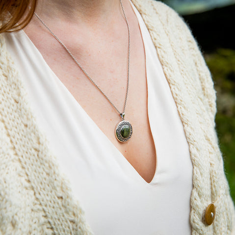 Person wearing a necklace with a green pendant, dressed in a white top and beige cardigan.