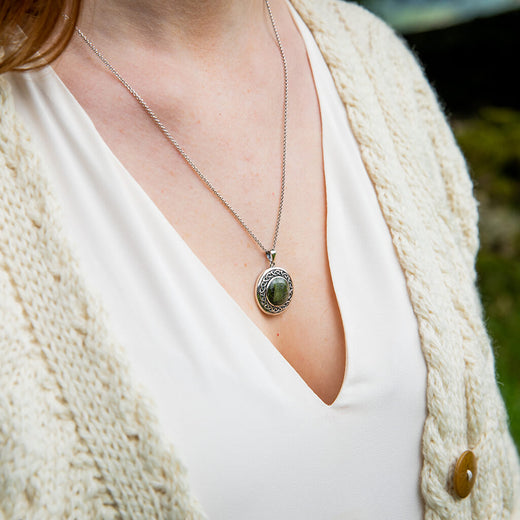 Person wearing a necklace with a green pendant, dressed in a white top and beige cardigan.