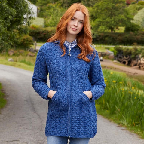 Woman wearing a blue Aran zipper cardigan standing on a path with greenery in the background