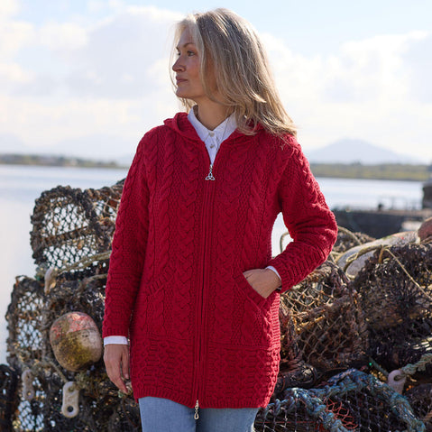 Woman wearing a red knitted Aran cardigan standing near fishing nets with a scenic background.