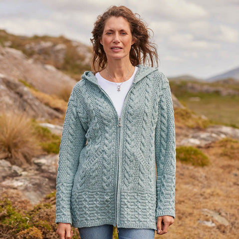 Woman wearing a teal knitted hoodie standing in a natural landscape.