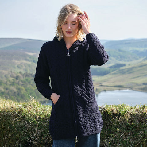 Woman wearing a navy Aran cardigan standing in a scenic outdoor setting with mountains and a lake.