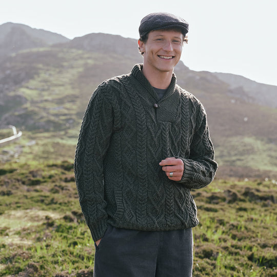 Image featuring the Men's Classic V-Neck One Button Aran Sweater in army green, crafted with authentic Irish Aran cable knit patterns and a signature one-button shawl collar, showcasing timeless Irish craftsmanship in a scenic countryside setting.