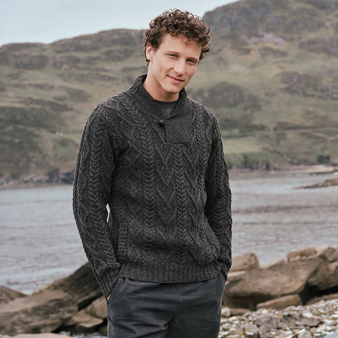 Image featuring the Men's Classic V-Neck One Button Aran Sweater in charcoal, crafted with authentic Irish Aran cable knit patterns and a signature one-button shawl collar, showcasing timeless Irish craftsmanship against a scenic coastal landscape.