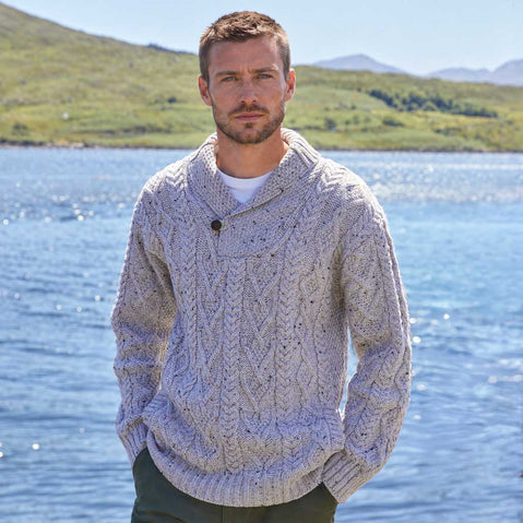 Image featuring the Men's Classic V-Neck One Button Aran Sweater in oatmeal, crafted with authentic Irish Aran cable knit patterns and a signature one-button shawl collar, showcasing timeless Irish craftsmanship against a scenic lakeside landscape inspired by Ireland's rugged countryside.