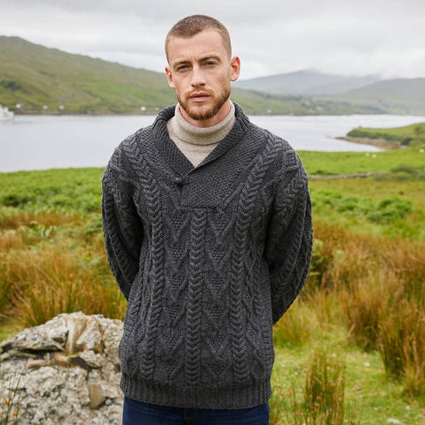 Man wearing a charcoal gray Aran sweater in a scenic outdoor setting with a lake and mountains.