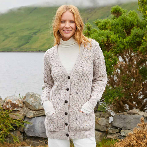Woman wearing a beige Women's Classic Aran Boyfriend Button-Front Cardigan standing by a lake with green hills in the background