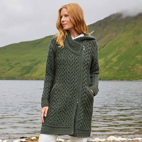 Woman wearing a green Women's Heritage Aran Hooded Zipper Coat standing by a lake with mountains in the background