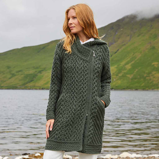 Woman wearing a green Women's Heritage Aran Hooded Zipper Coat standing by a lake with mountains in the background