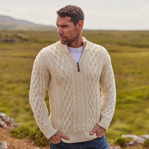 Man wearing a cream cable knit Aran sweater in a natural landscape