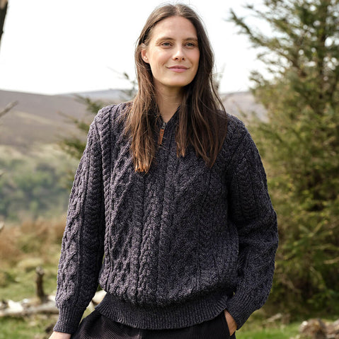 Woman wearing a dark gray cable knit sweater standing outdoors with greenery in the background