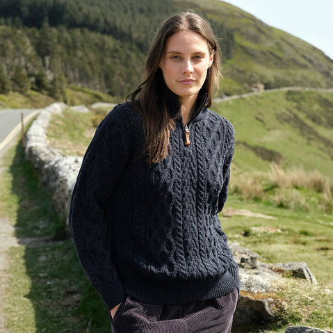 Woman wearing a dark blue knitted sweater standing on a road with green hills in the background