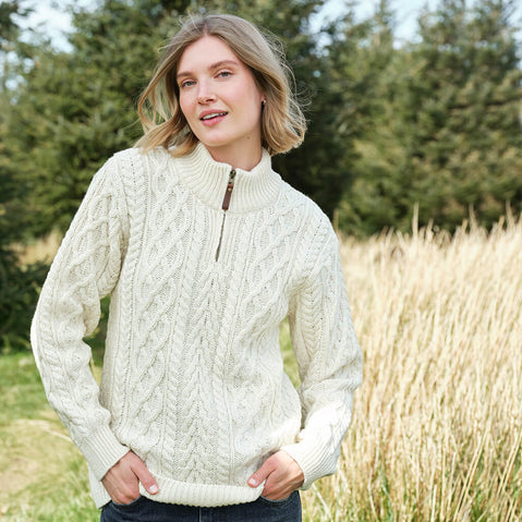 Woman wearing a cream Aran sweater standing outdoors with trees and grass in the background