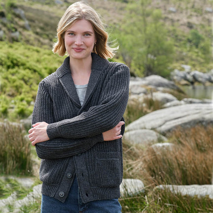 Woman wearing a dark gray Aran cardigan in a natural setting with greenery and rocks.