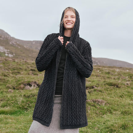 Image featuring the Women's Signature Hooded Aran Waterfall Cardigan in charcoal, crafted with authentic Irish Aran cable knit patterns, a flowing waterfall silhouette, and a comfortable hood, showcasing timeless Irish craftsmanship in a scenic countryside setting.