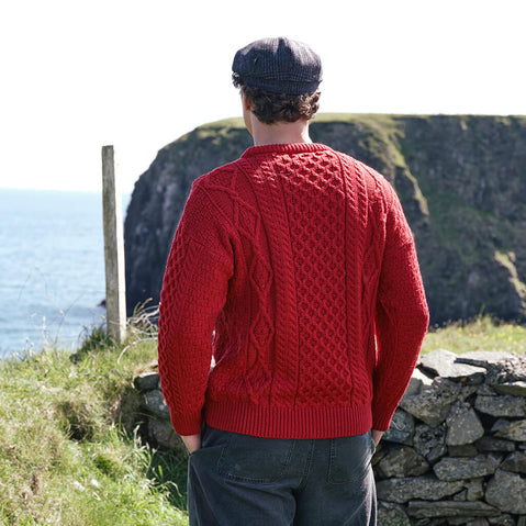Back view of the Men's Fisherman Lightweight Crew Neck Heritage Sweater in Cranberry Red, showcasing intricate traditional Irish cable knit stitching and authentic heritage craftsmanship against the dramatic Irish coastline.