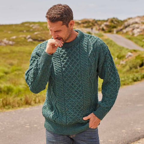 Man wearing a green Men's Fisherman Lightweight Crew Neck Heritage Sweater standing on a road with a natural landscape in the background