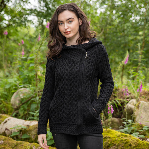 Woman wearing a black cable knit Aran hoodie in a forest setting
