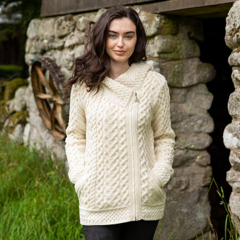 Woman wearing a cream knitted sweater standing in front of a stone wall.