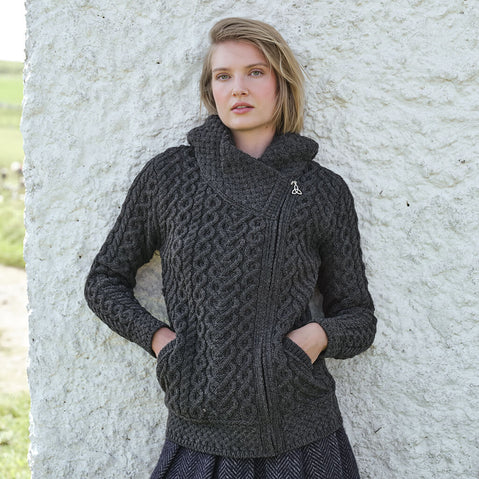 Women's Signature Aran Celtic Zipper Hooded Cardigan in Charcoal, featuring traditional Irish cable knit stitching, a Celtic-inspired zip design, and a cozy hood, styled beside a traditional Irish cottage showcasing authentic Aran craftsmanship.