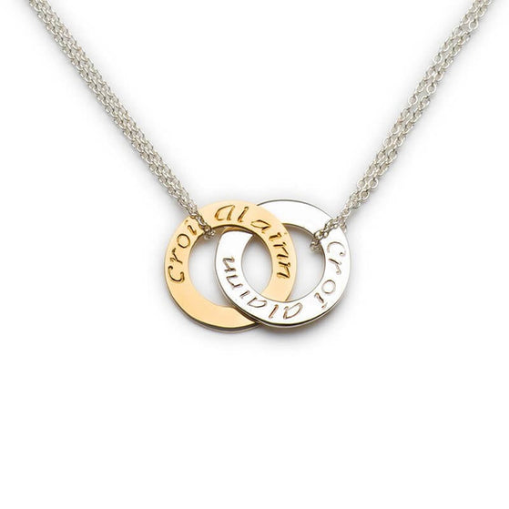 Close-up of an Irish Croí Álainn pendant necklace with two interlocking circles—one gold-toned engraved with “croí” and one silver-toned engraved with “álainn”—on a delicate silver chain. Symbolic Irish jewelry representing a beautiful heart.