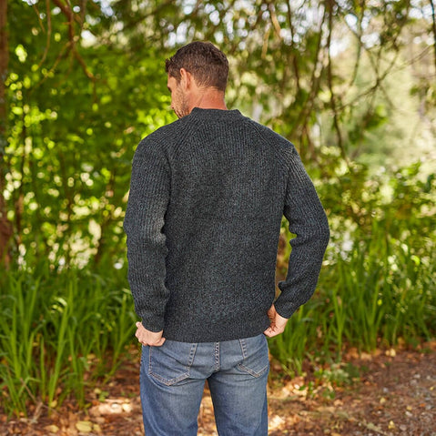 A man standing back view in a forest wearing a gray half-zip Irish sweater with a plain stitch design.