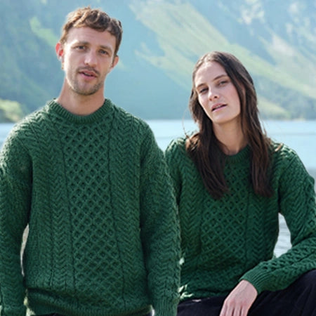 Two people wearing green knitted sweaters by a lake with mountains in the background