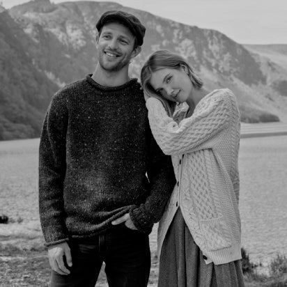 Black and white photo of a couple wearing Irish Aran Sweaters standing together with a mountainous background