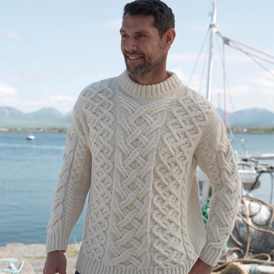 A man wearing a cream Aran sweater with a geometric pattern standing outdoors.