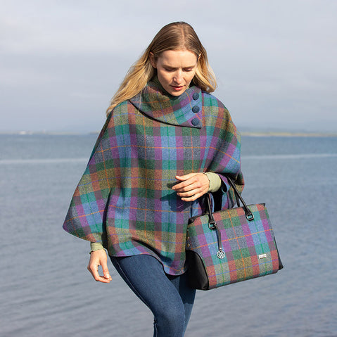 A handbag with a tweed body and vegan leather details, placed on a stone surface with foliage in the background.