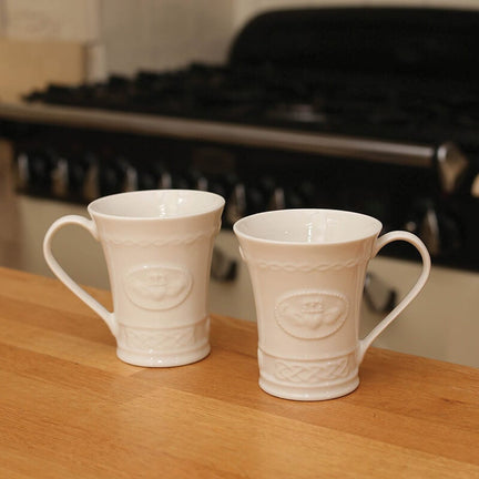 Irish home décor. Two white ceramic mugs with Celtic knot designs and Claddagh symbols, placed on a kitchen counter.