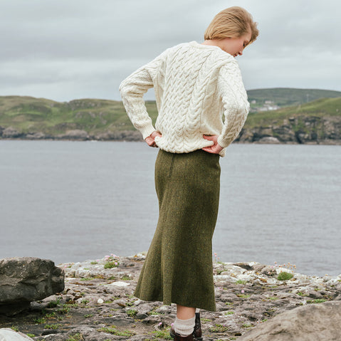 Image featuring the Irish Tweed Fleck A-Line Skirt in green, crafted from authentic Irish flecked tweed with a flattering A-line shape, showcasing timeless Irish heritage style from a rear view against a scenic coastal landscape.