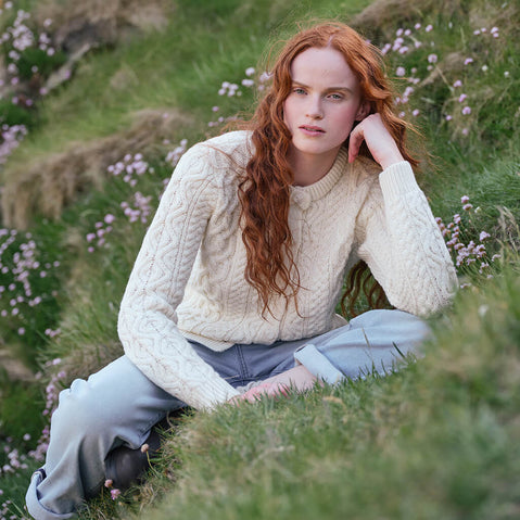 Image featuring the Women's Button Front Short Aran Cardigan in natural, crafted with authentic Irish Aran cable knit patterns and classic button-front detailing, showcasing timeless Irish craftsmanship in a scenic coastal landscape.