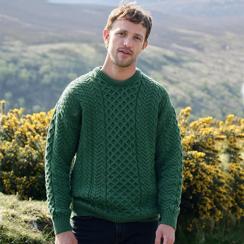 Man wearing a green Aran sweater standing outdoors with a scenic background
