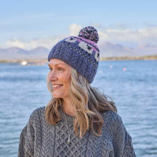 A woman wearing a knitted bobble hat with a geometric sheep design in pink and blue colors.