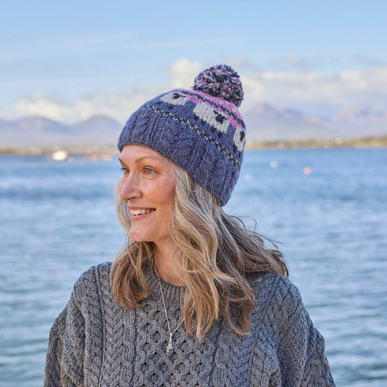 A woman wearing a knitted bobble hat with a geometric sheep design in pink and blue colors.