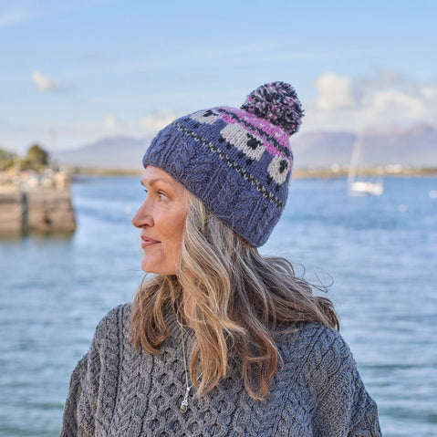 A woman wearing a knitted bobble hat with a geometric sheep design in pink and blue colors.